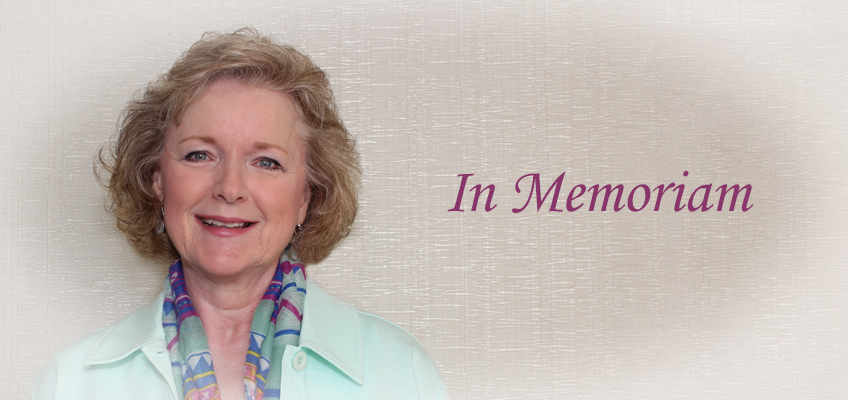 A smiling woman with short, curly hair wears a light-colored jacket and a colorful scarf. The text In Memoriam is written in purple on the textured background to her right.