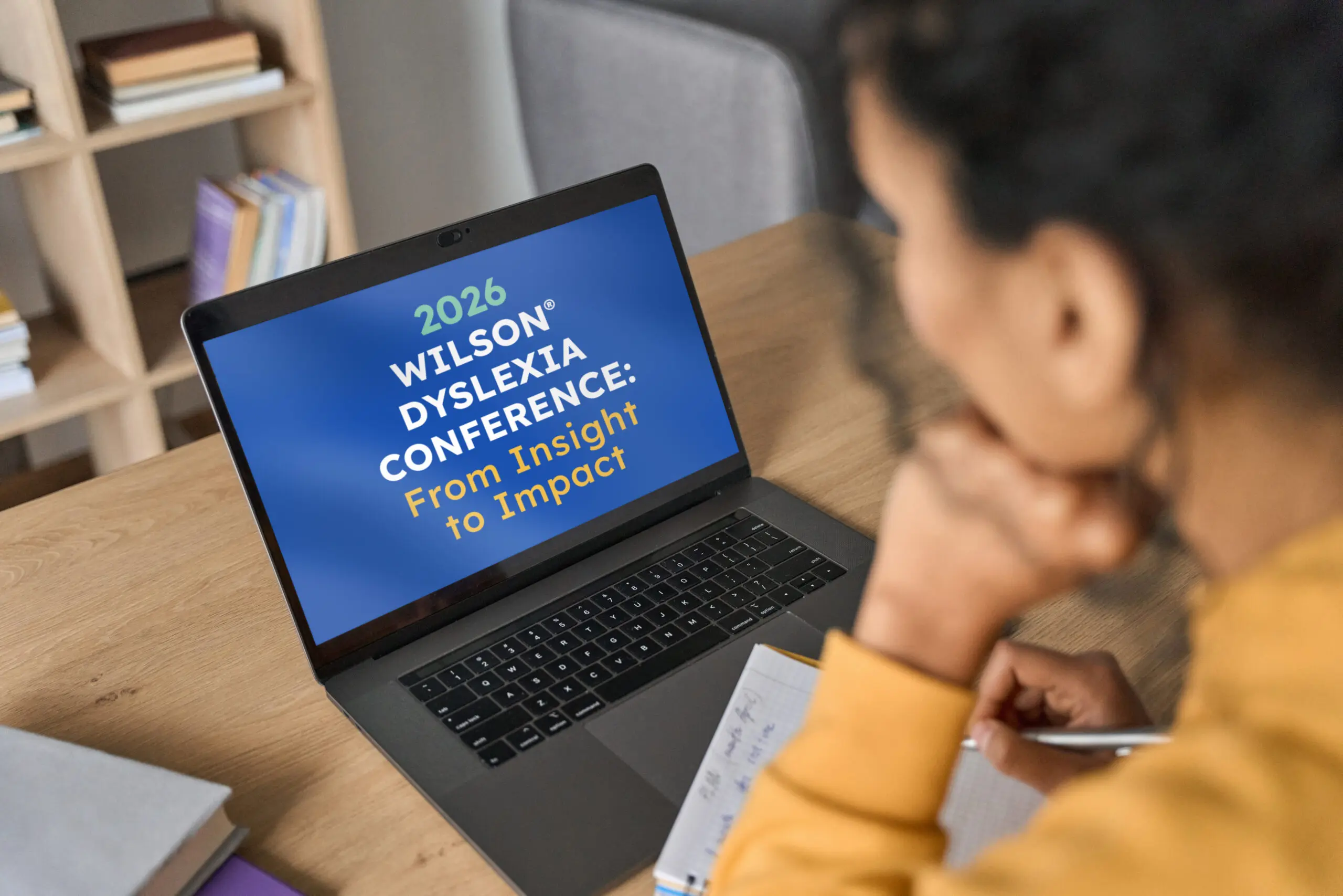 a person taking notes in front of their laptop with the screen open