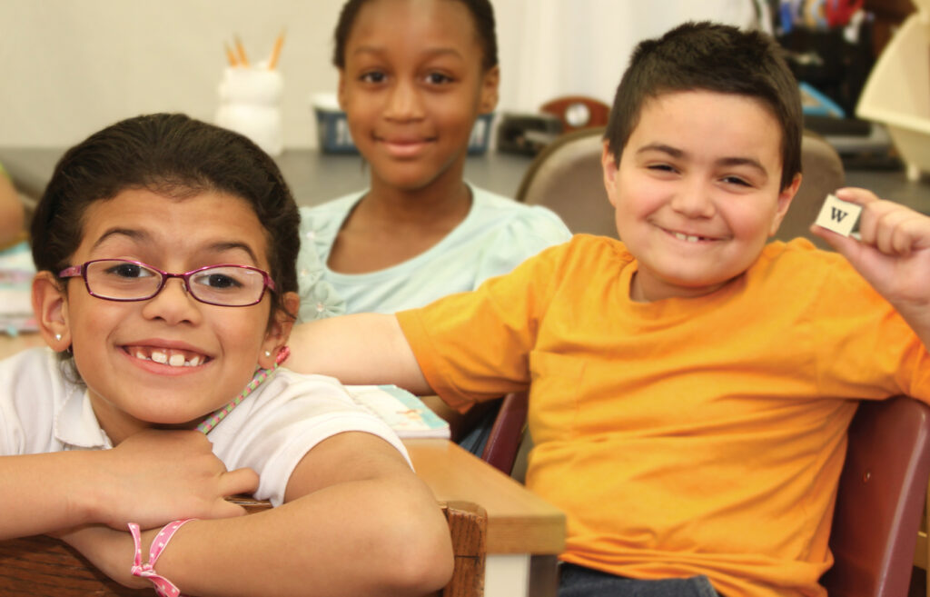 3 smiling students with one boy holding up a "w" magnetic letter tile