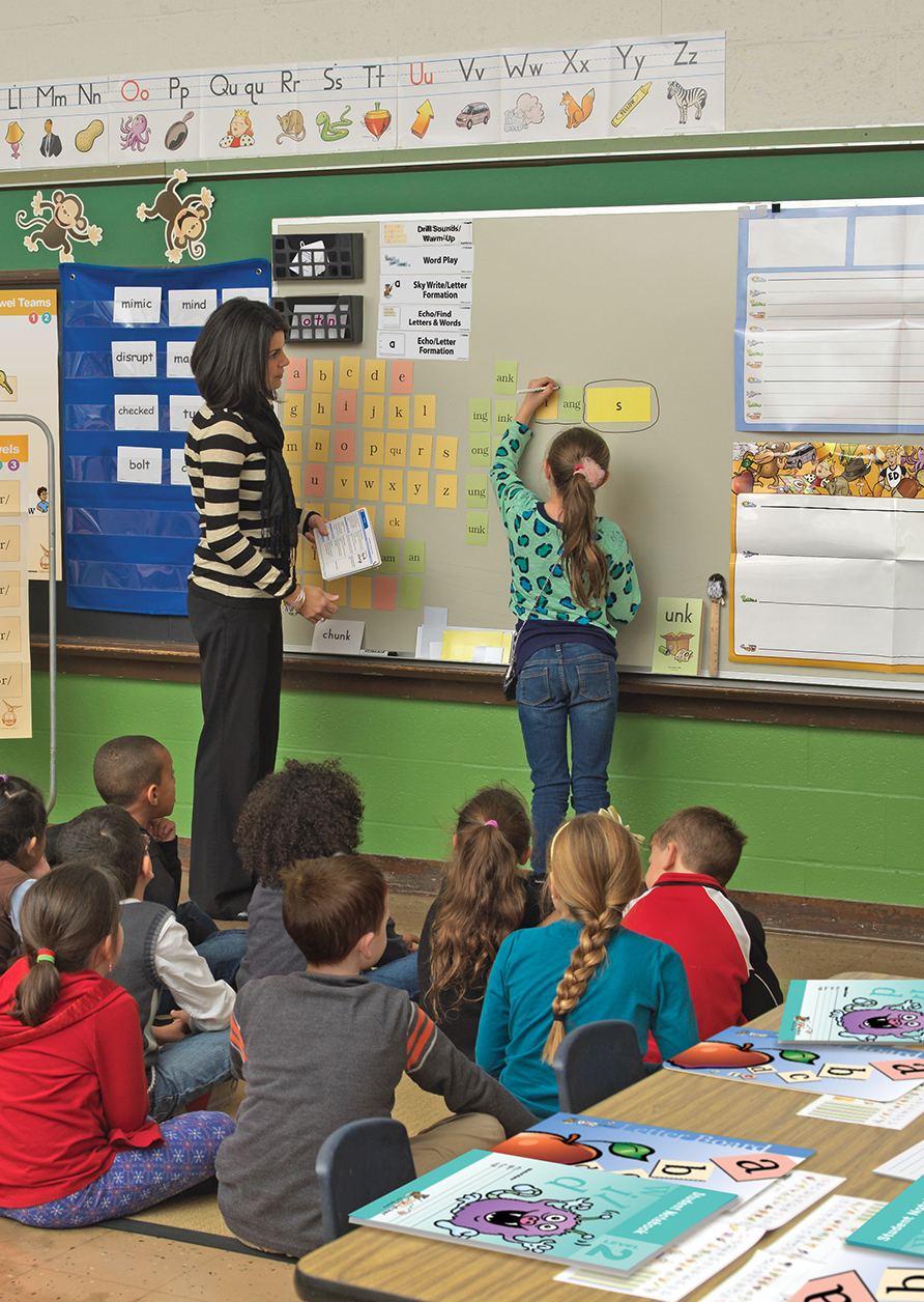 Fundations_Materials_Fun_classroom_892x1256 Teacher with student at white board marking up a word