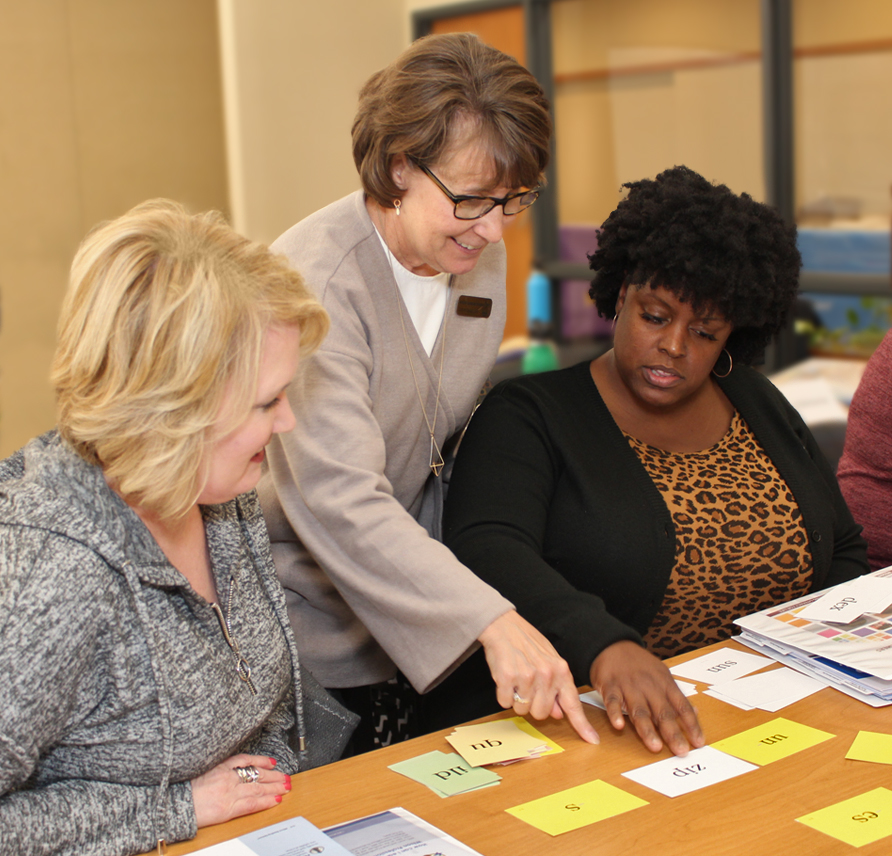 Workshop presenter pointing to syllable cards between two workshop participants. 