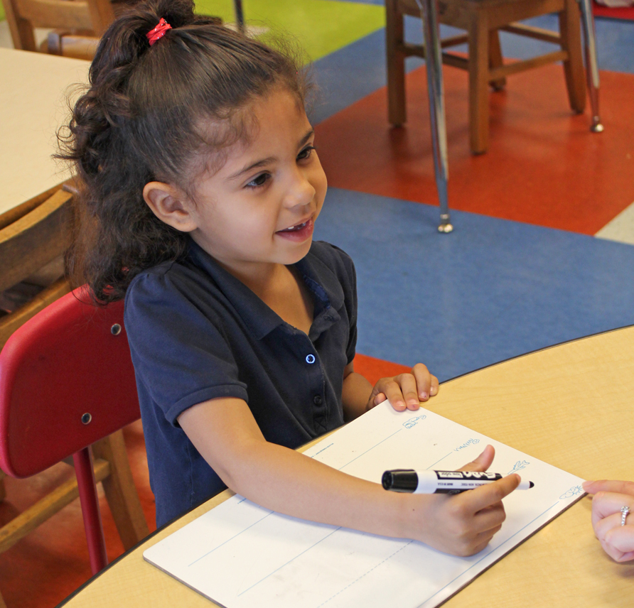 Young girl smiling as she holds a dry erase marker