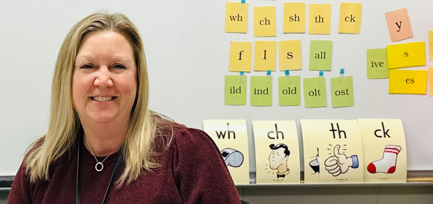 Woman smiling in front of whiteboard containing Fundations letter and syllable cards