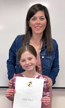 Child holding certificate as a woman stands behind her.