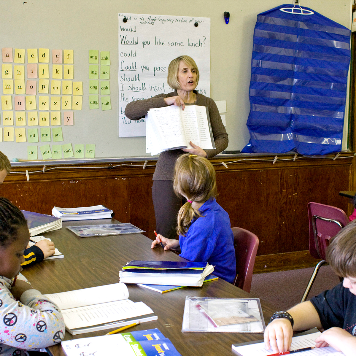 Teacher standing at white board showing a book to students 