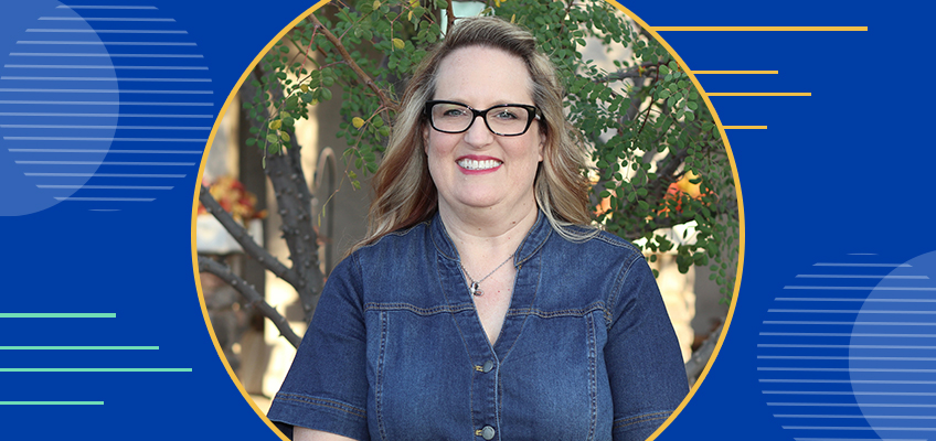 Cassie Bates smiles while posing outdoors in front of a tree with green leaves. She is wearing a denim dress and black-framed glasses. The background of the image is framed within a circular border, surrounded by a blue and gold graphic design with abstract lines and circular elements.