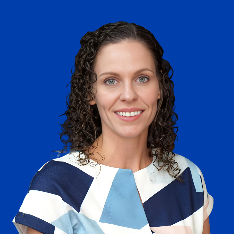 Woman with long curly brown hair and wearing a white shirt with geometric blue shapes on her shirt.