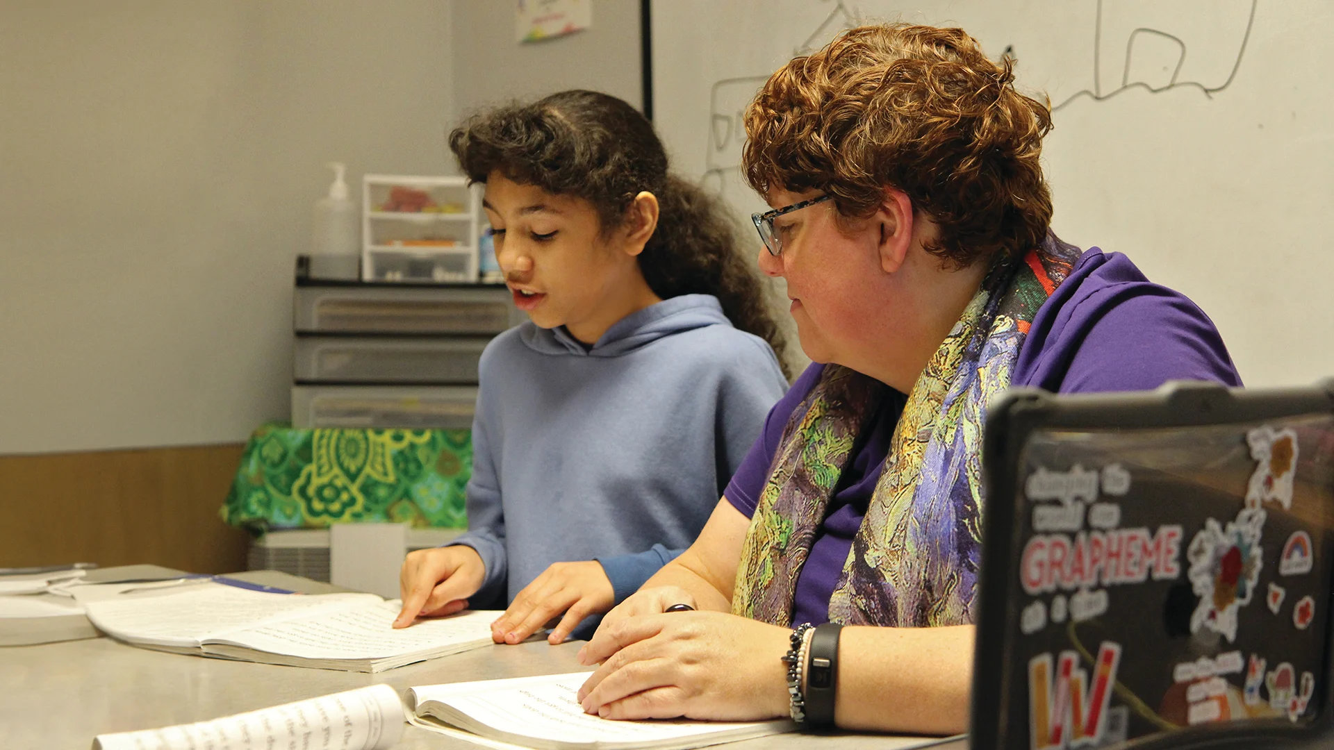 Teacher helps student with reading, focusing on words and graphemes.