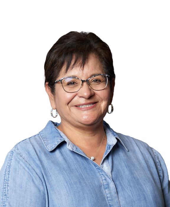 A woman smiling with short hair, earings and glasses wearing a blue button down shirt.