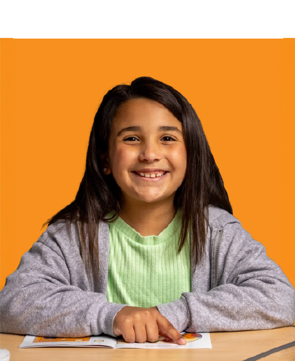 Smiling girl sits at a desk, pointing to a page in front of her, with an orange background behind her.