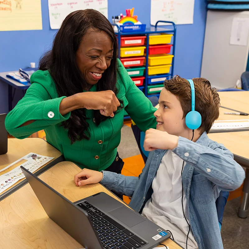 Teacher and student fist bump over laptop during Fundations webinar.