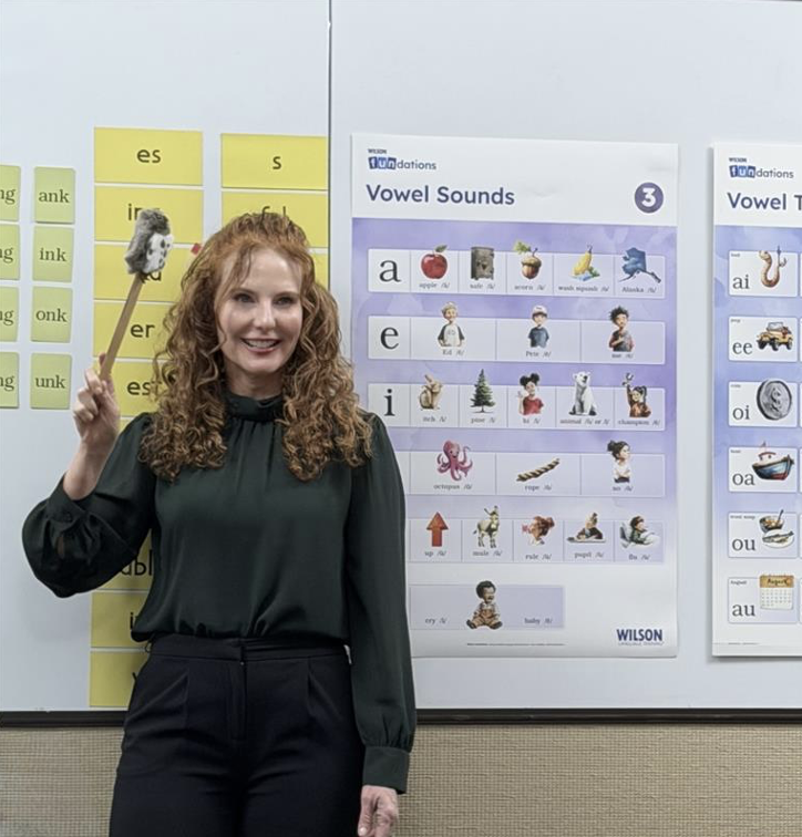 Teacher standing in front of an educational poster hanging on a white board