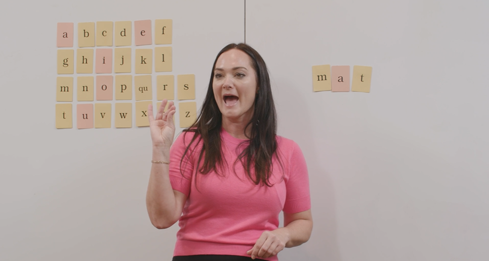 Teaching standing in front of a whiteboard with letter flash cards on it