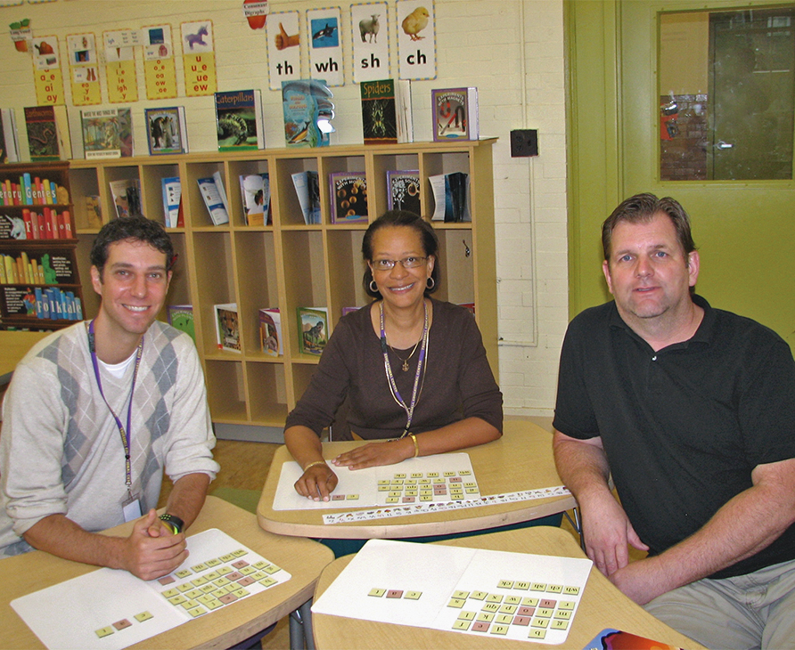 Three adults at tables with Scrabble tiles, likely a facilitator certification event.