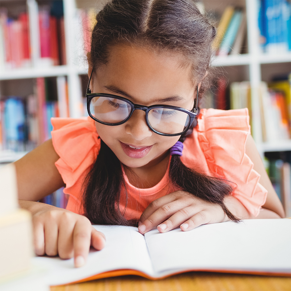Young girl with glasses reading a book in a library