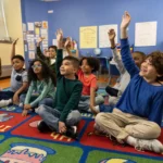 Children raising hands in a classroom, engaged in Acadience Learning.