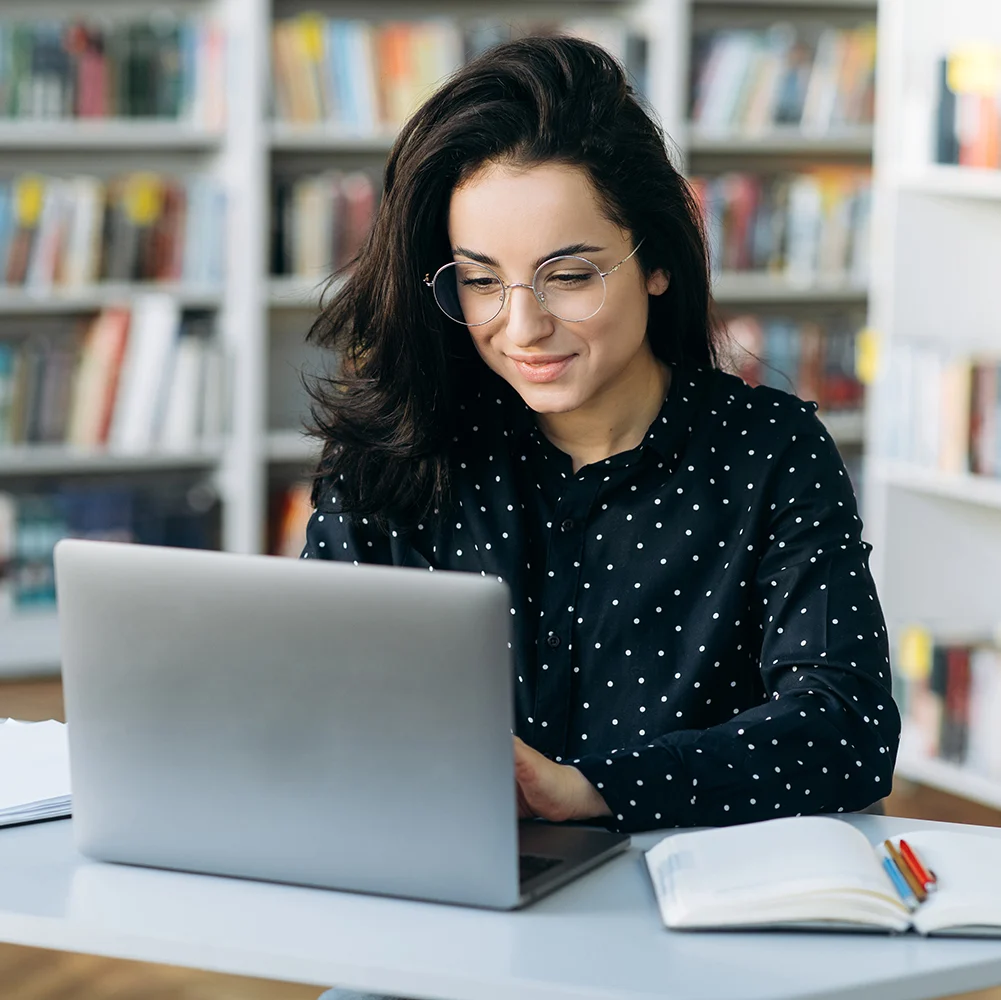 Woman with glasses on a laptop in a library